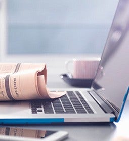 Closeup of a laptop with the newspaper over the keyboard with a cup of coffee in the background.