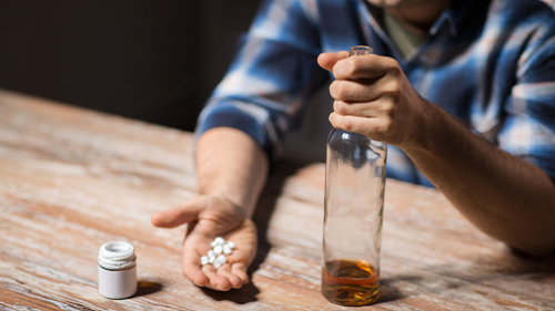 depression, drug abuse and addiction people concept - unhappy drunk man with bottle of alcohol and pills