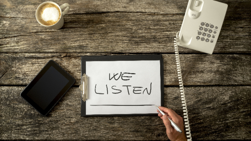 We listen sign on wooden desk with telephone, digital tablet and cup of coffee.