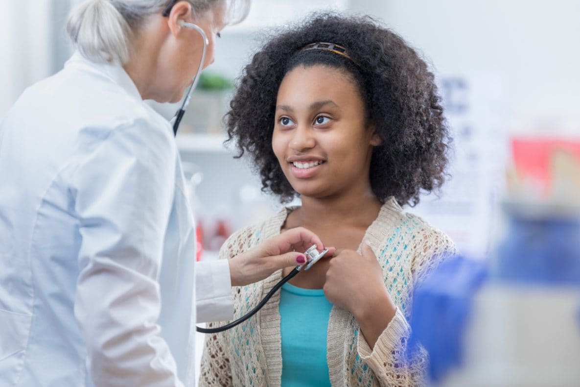 School nurse using stethoscope to examine young female student.