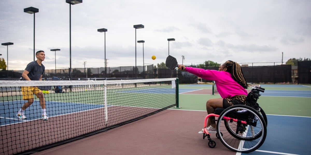 A young black disabled woman playing pickleball with her friend.