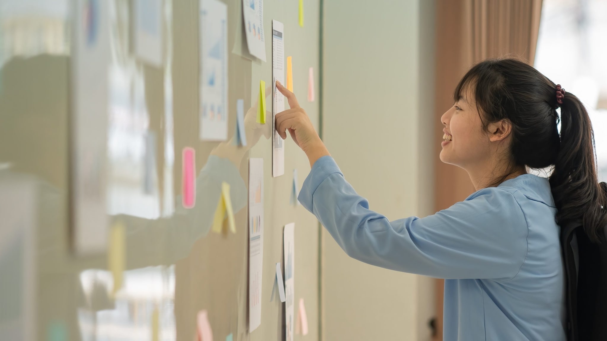 Asian American woman reads notice on notice board.