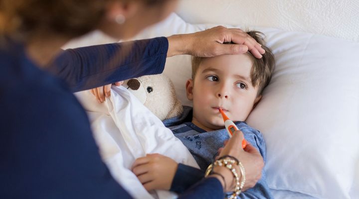 Una madre tomándole la temperatura a su hijo mientras está acostado en la cama.