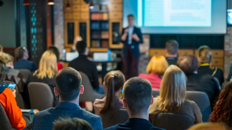 A group of people in a course sitting in seats listening to an instructor up front