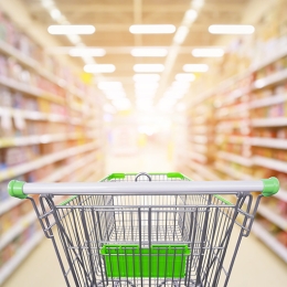 Supermarket aisle product shelves interior blur background with empty shopping cart