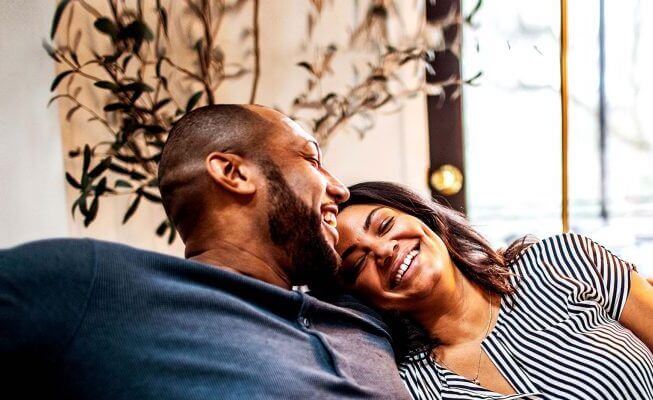 Couple sitting on couch smiling and laughing.