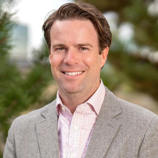 Man in tan suit jacket posing for portrait.