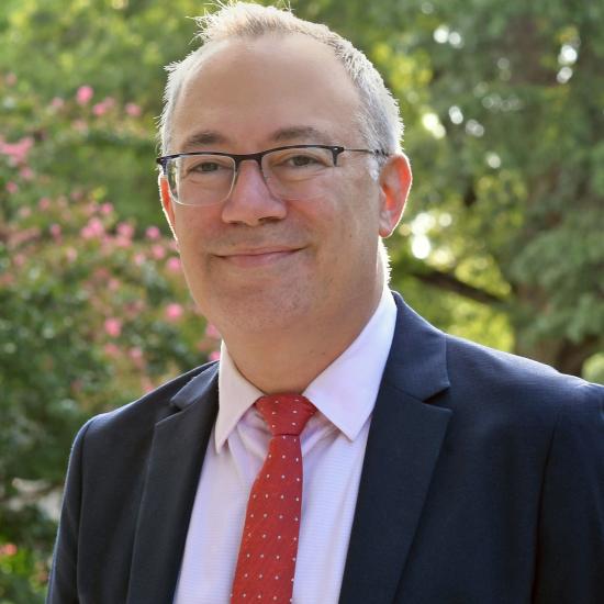 Portrait of man wearing suit, red tie, and glasses. 