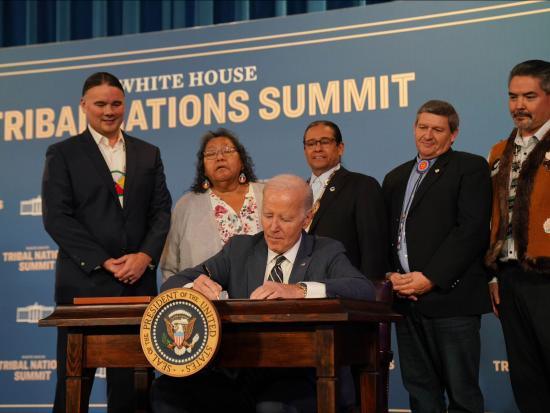 President Biden signing paper at table with 5 others standing behind him