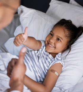 Little girl lying down on bed, thumb up