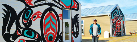 Male CO-OP student posing for a picture near a mural with indigenous art in Whitehorse, Yukon