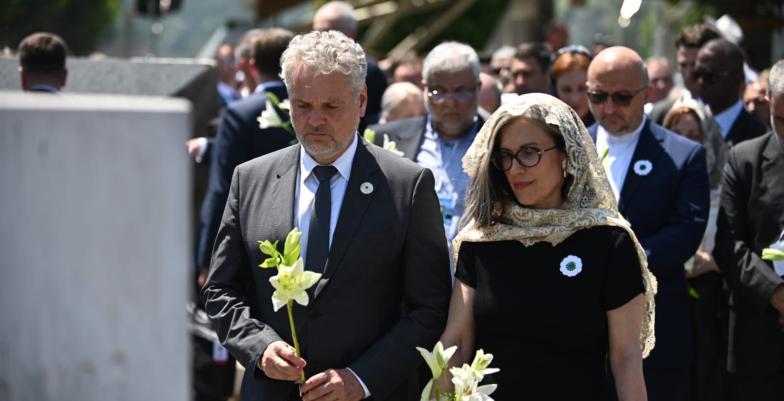 A man and a womon at a commemoration ceremony in solemn pose. 