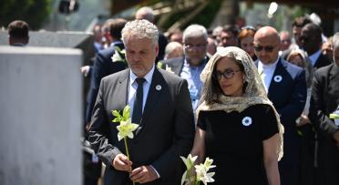 A man and a womon at a commemoration ceremony in solemn pose. 