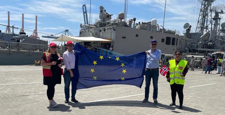 People hold EU flag with naval ship in background