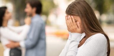 A woman crying in her hands with a couple about to kiss in the background