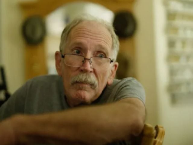 Older man sitting in diner at table, looking at camera