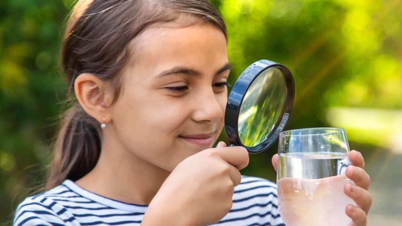 Young girl looking at a glass of water through magnifying glass