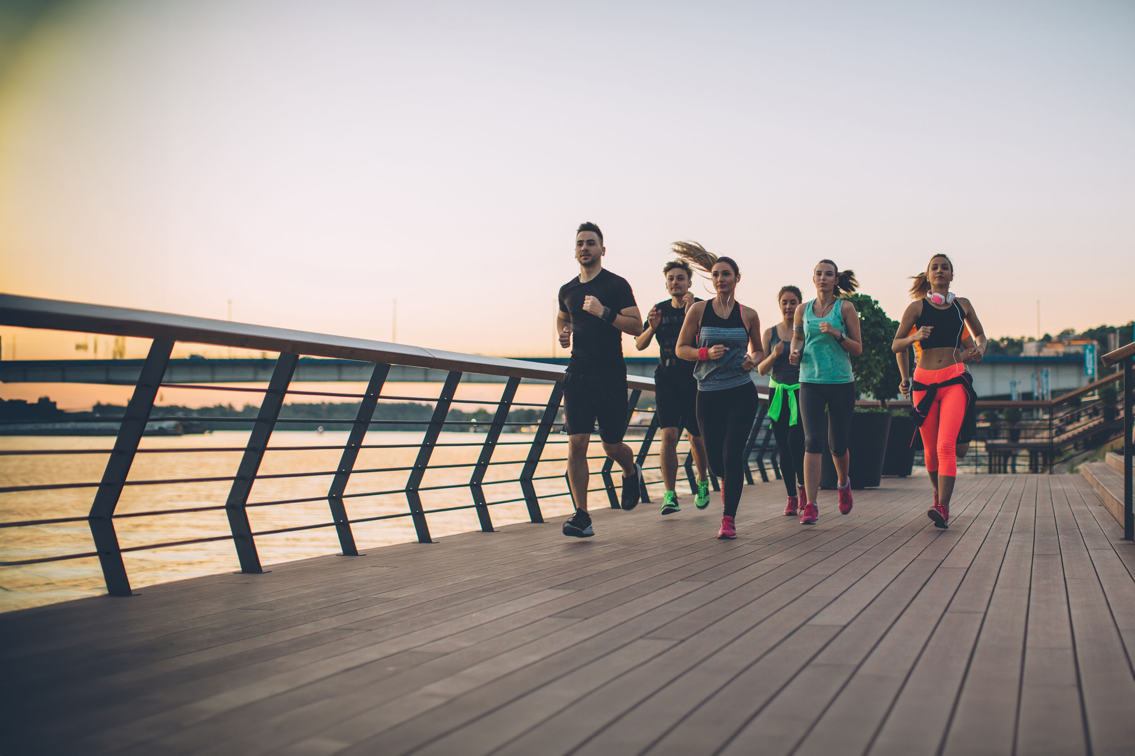 Group of young men and women jogging on path next to a river