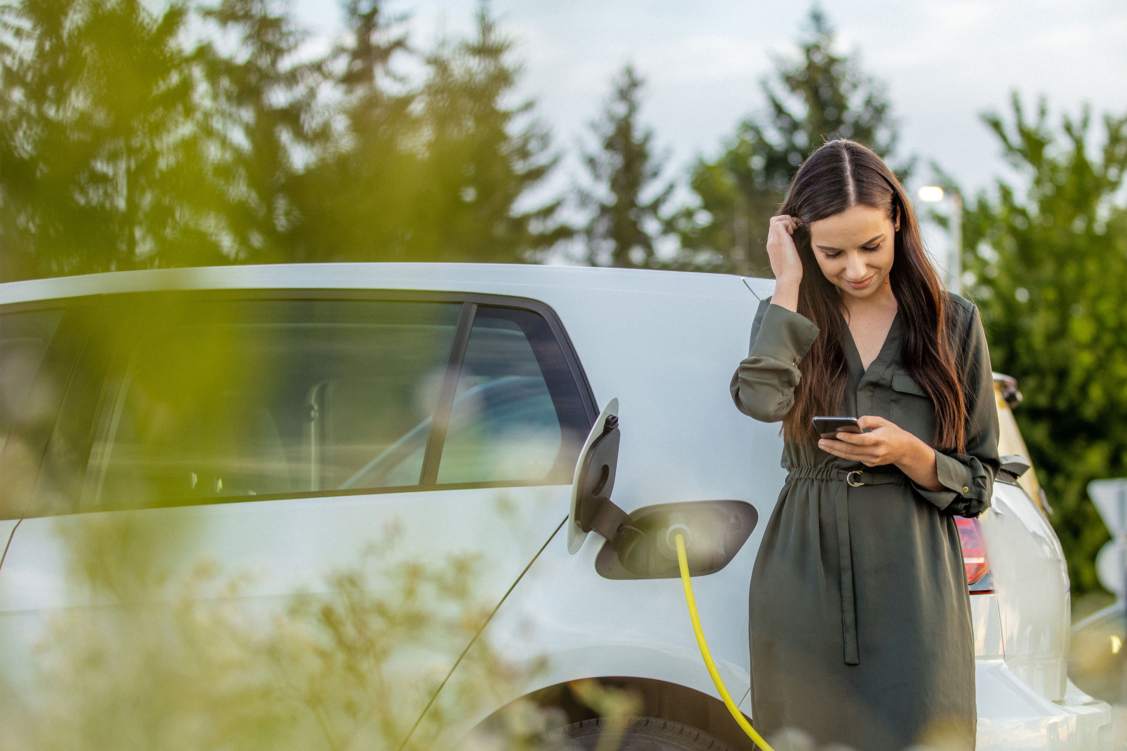 Woman using mobile phone while waiting for electric car to charge