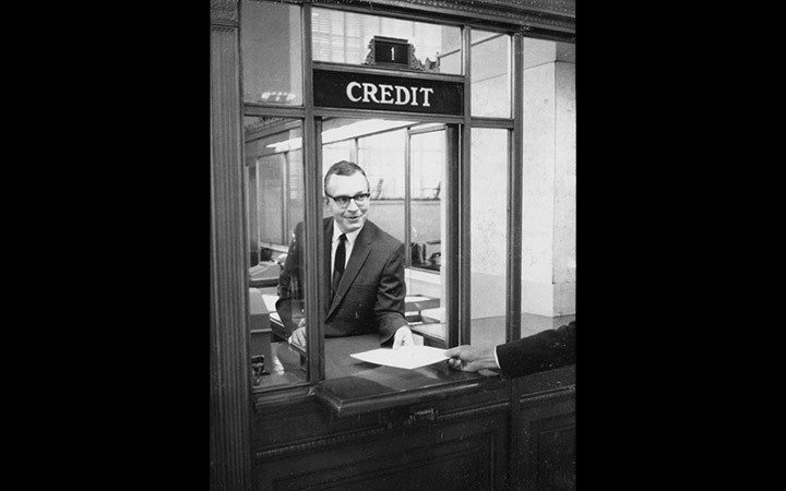 Bernie Berns hands paper through the Credit window on the first floor of the Federal Reserve Bank of St. Louis, 1967 (via <a href="https://fraser.stlouisfed.org/archival-collection/federal-reserve-bank-st-louis-centennial-5182/credit-discount-window-st-louis-fed-photograph-527398">FRASER</a>)