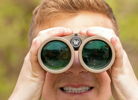 A red-haired boy looks at the camera through binoculars.