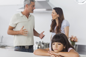 A girl sitting at a table while her parents argue behind her.