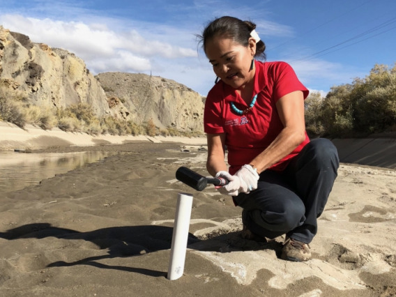 Woman in a river bed collecting a soil sample