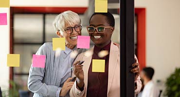 two women adding post it stickies to a glass wall