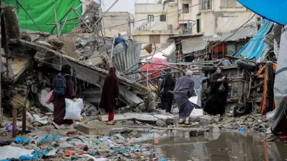 People crossing the road in front of a commercial shop destroyed during the war