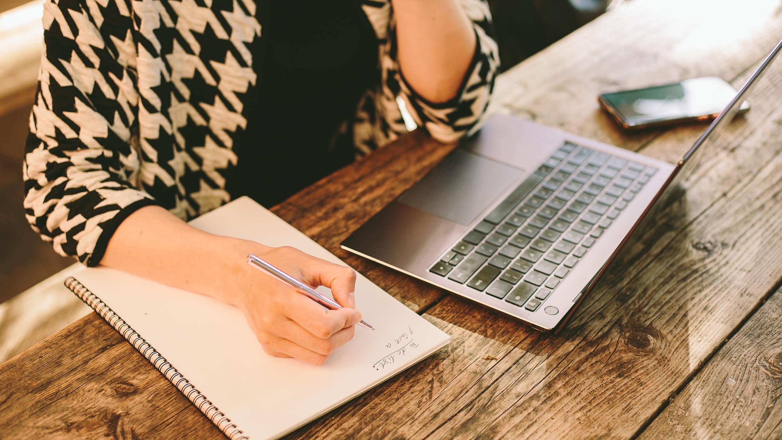 Person looking at laptop and taking notes on a notebook