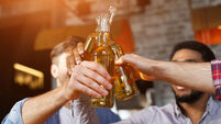 Male Friends Drinking Beer And Clinking Bottles At Bar