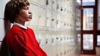 Schoolboy (11-13) sitting in corridor leaning head on wall, side view