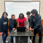 man surrounded by students around a computer