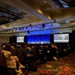 photo of a dark conference hall where someone presents on a screen