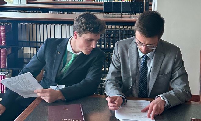 Two male students sharing a book in a legal library.