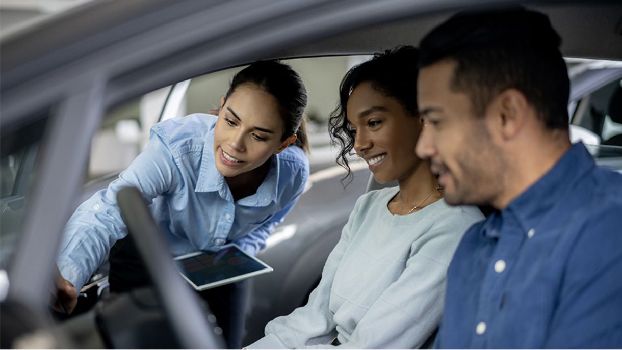 Car sales woman showing features to couple