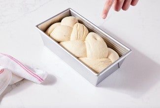 Braided bread dough in loaf pan, with visible indention from poke test