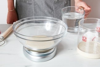 Bowl of sourdough starter on scale next to a crock with sourdough starter