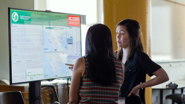 Two researchers discuss maps shown on a screen.