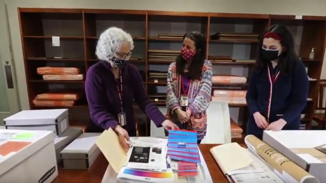 Three people at a table looking at folders, papers, and boxes of special collections materials