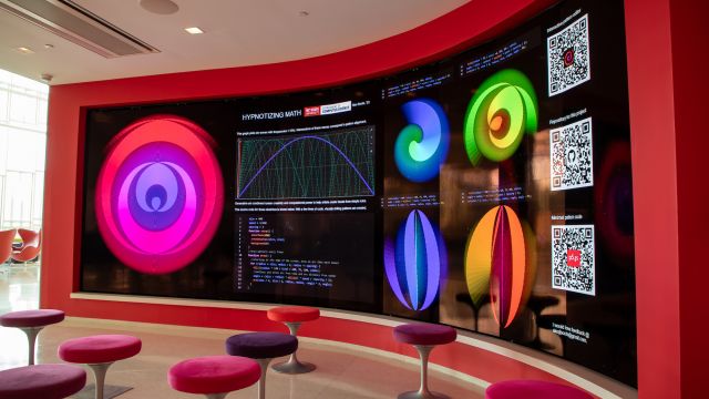 Stools in front of the large, curved screen of the Immersion Theater. The screen shows visuals from an exhibit called "Hypnotizing Math."