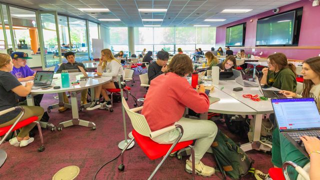 Many students sit at tables in a very full Fishbowl Forum 