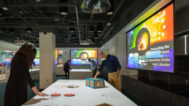 People in a low-lit gallery hovering their hands over tables with physical and projected digital exhibits