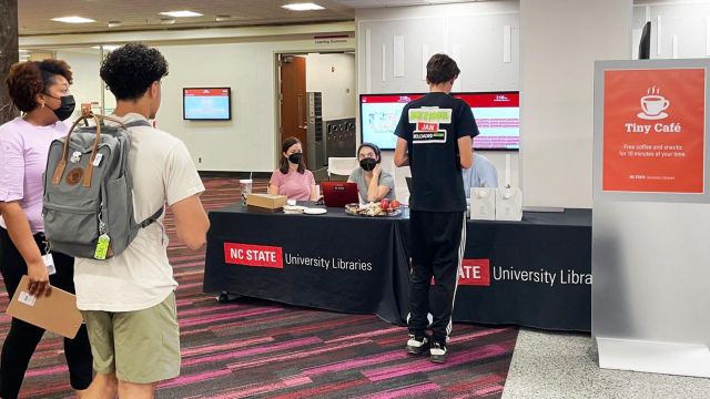 Students line up in front of a table that has coffee, pastries, and a laptop on it