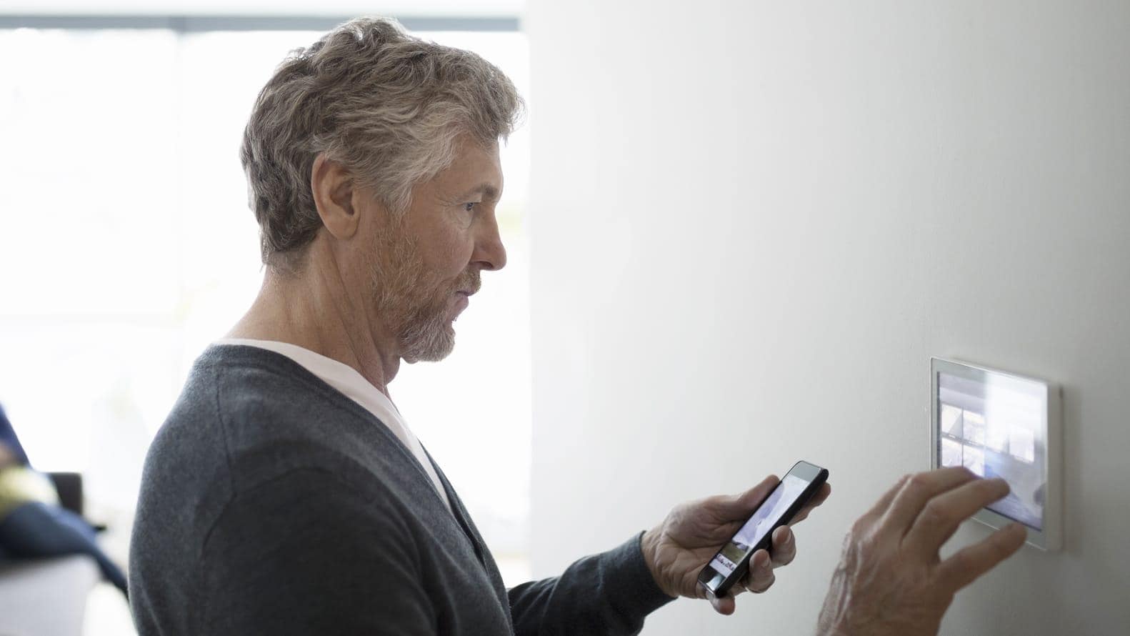 Man holding a smartphone and programming a device on the wall 