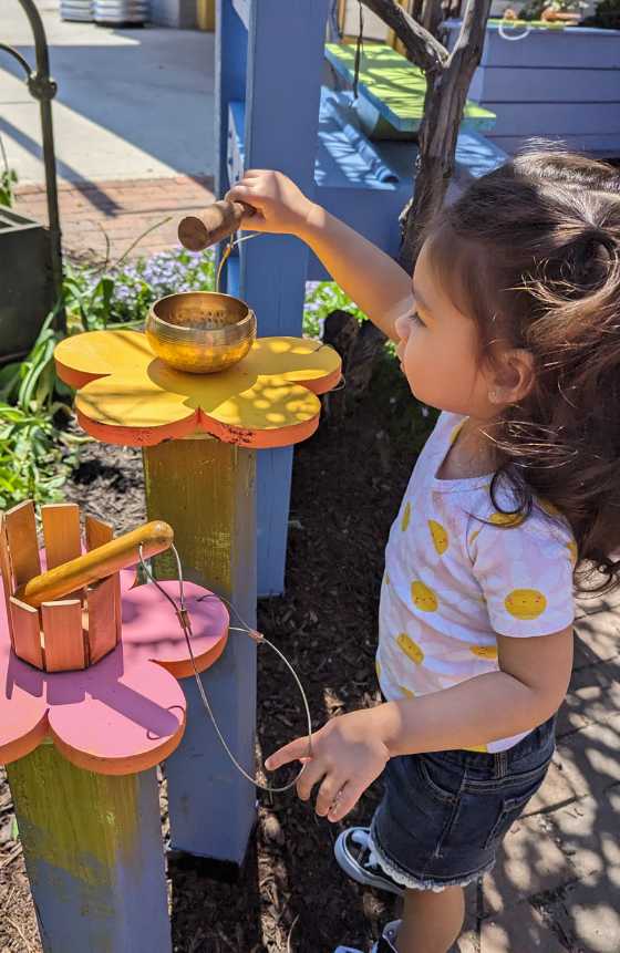 A child standing outside in LICM's Backyard while playing a drum with a mallet. 