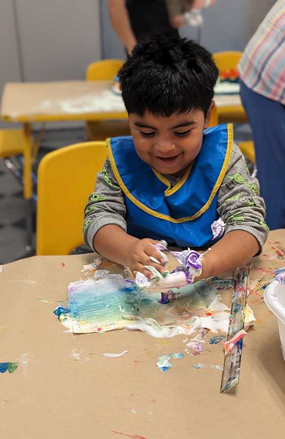 A child sitting at a table wearing a smock while playing with slime. 