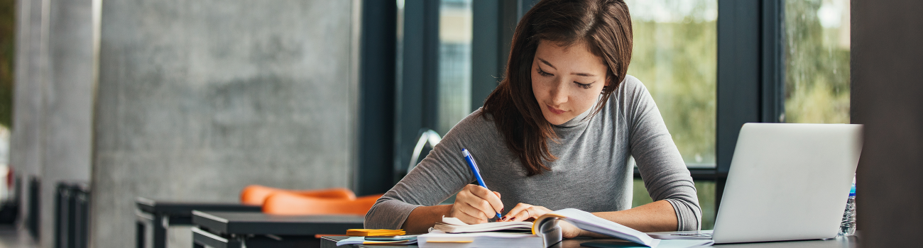 Person taking notes at desk with laptop