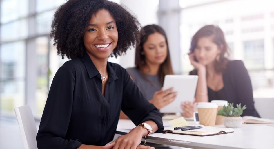 Law student smiling at the camera with two other students studying in the background