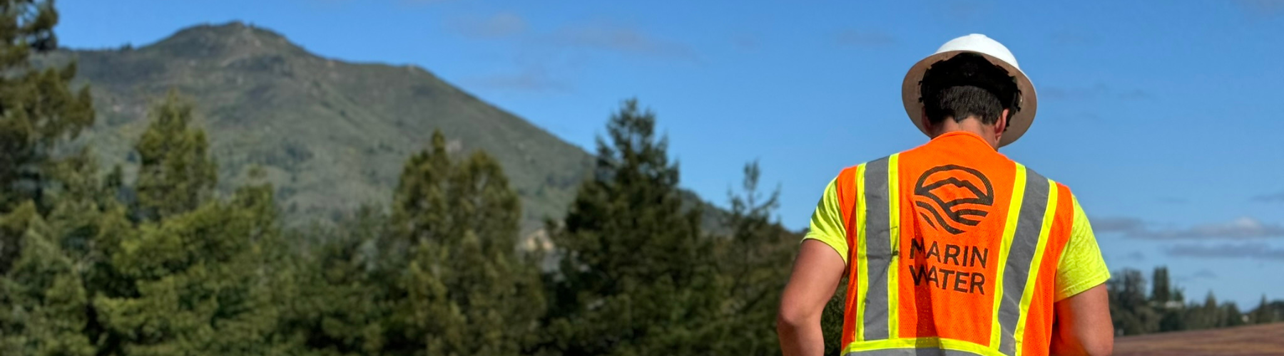 A worker in a hard hat and safety vest with the text "Marin Water" faces a mountain.